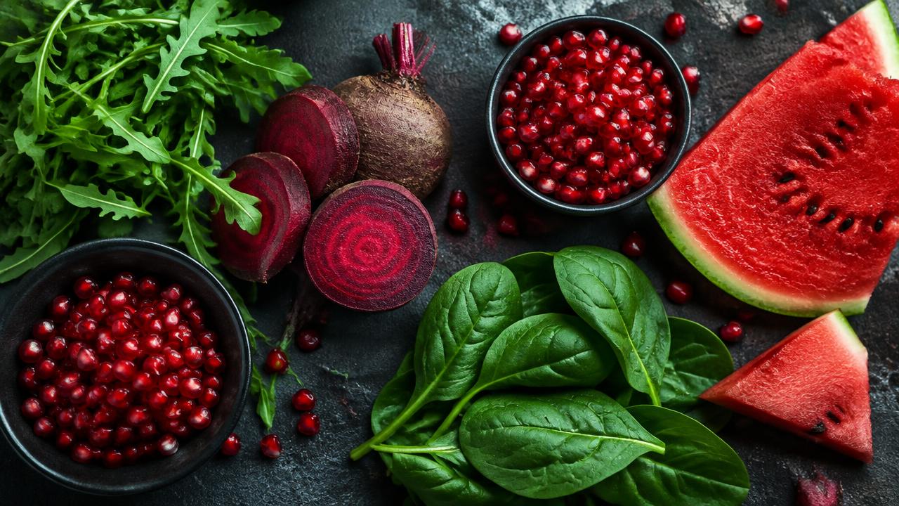 Beetroot, arugula, spinach, pomegranate and watermelon arranged on a dark stone board
